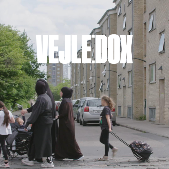 Stillbillede fra filmen som viser mennesker med kufferter foran boligblok.