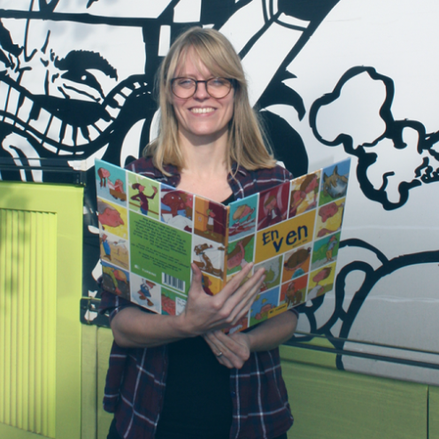 Børnebibliotekaren Anne ved siden af bussen med en billedbog.