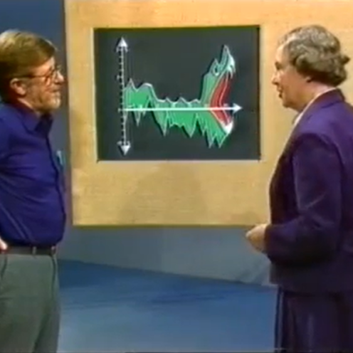 Ældre tv-klip med to personer, der taler foran en grafisk illustration.